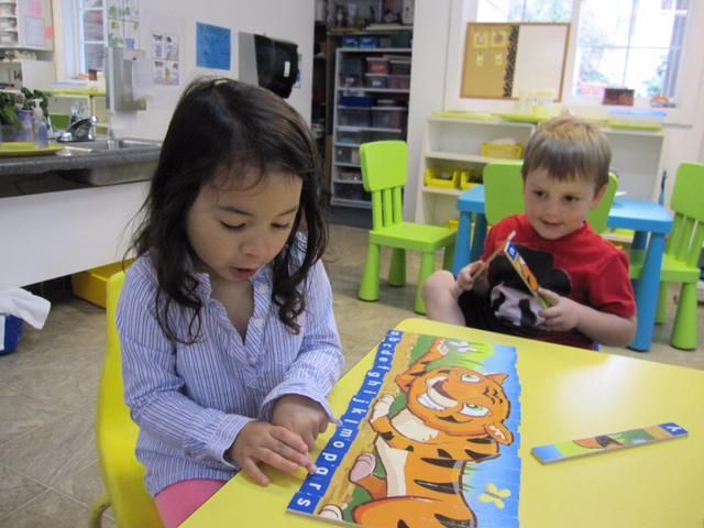 Girl and boy at yellow table, assembling a tiger puzzle in a classroom