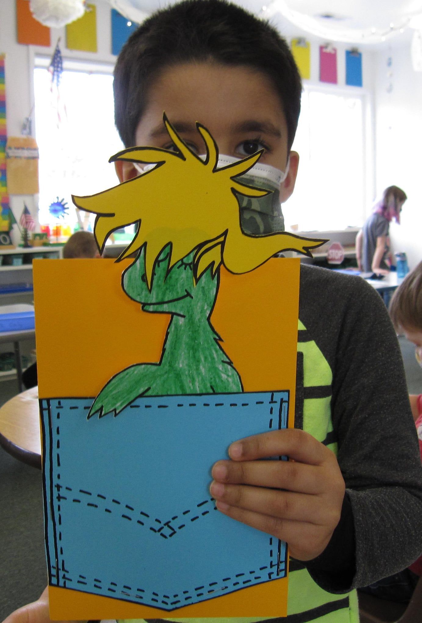Boy holding a handmade card featuring a green creature in a blue pocket