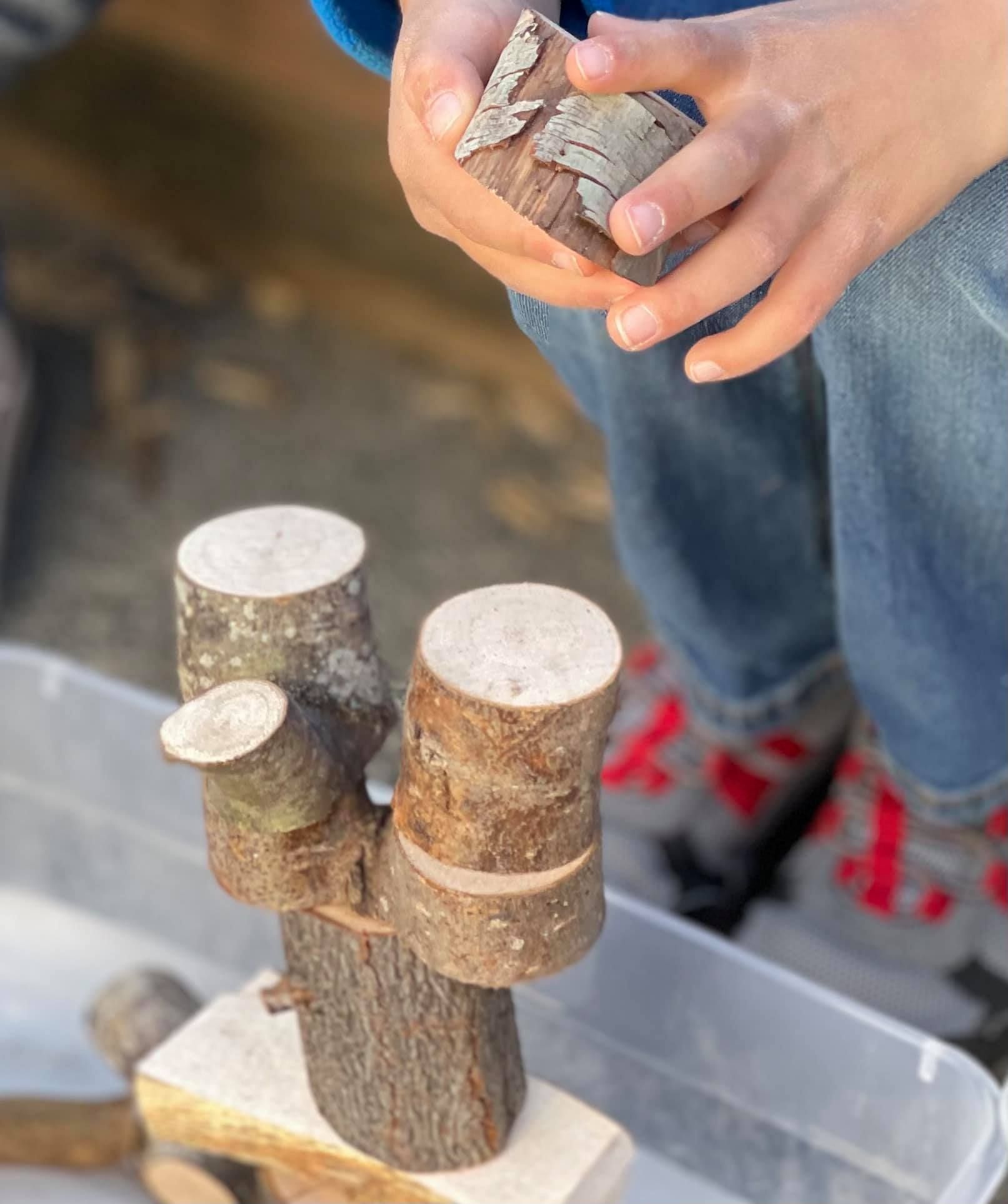 Child stacking wooden blocks and tree pieces outside