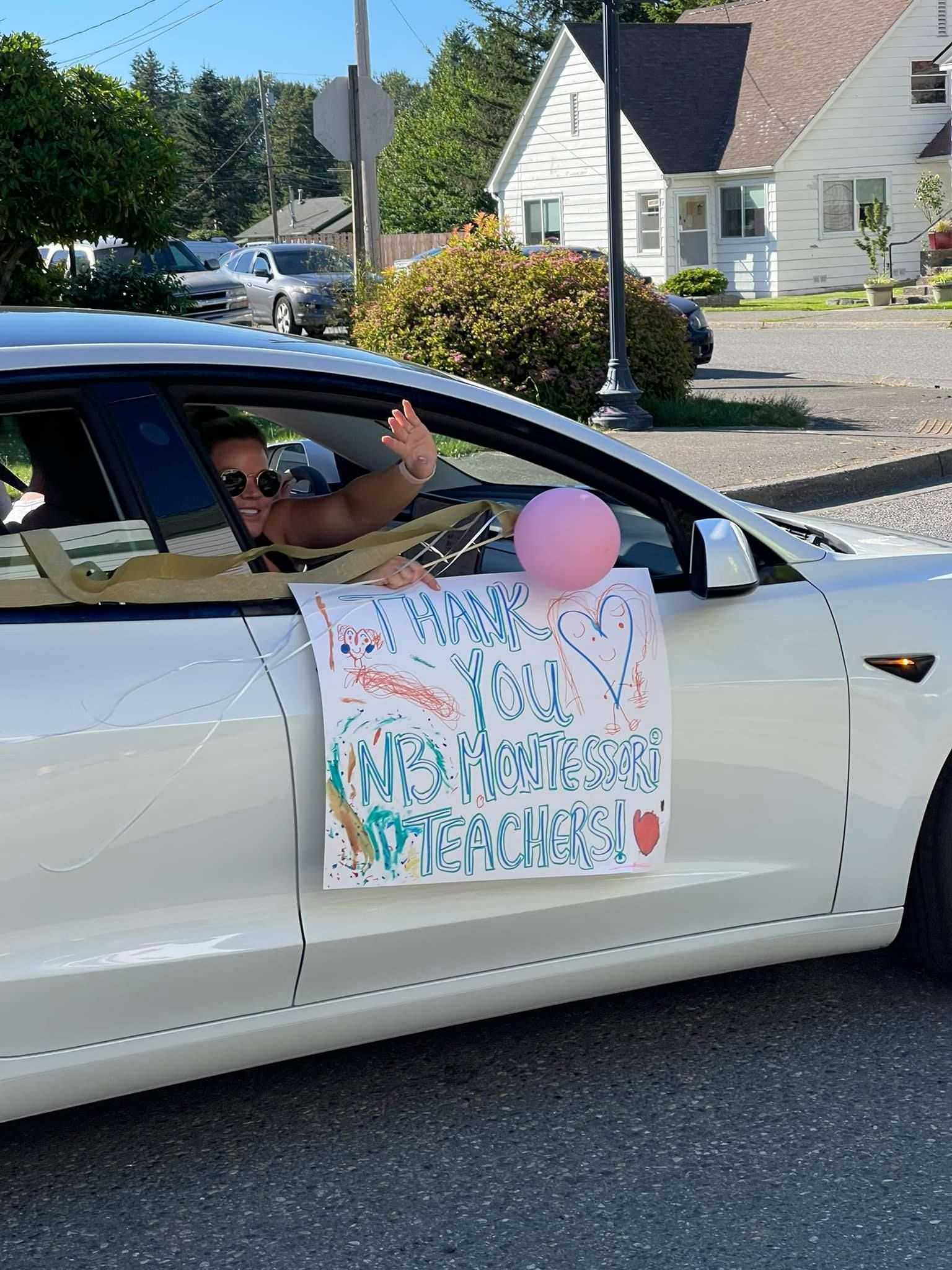 A woman waves from a white car