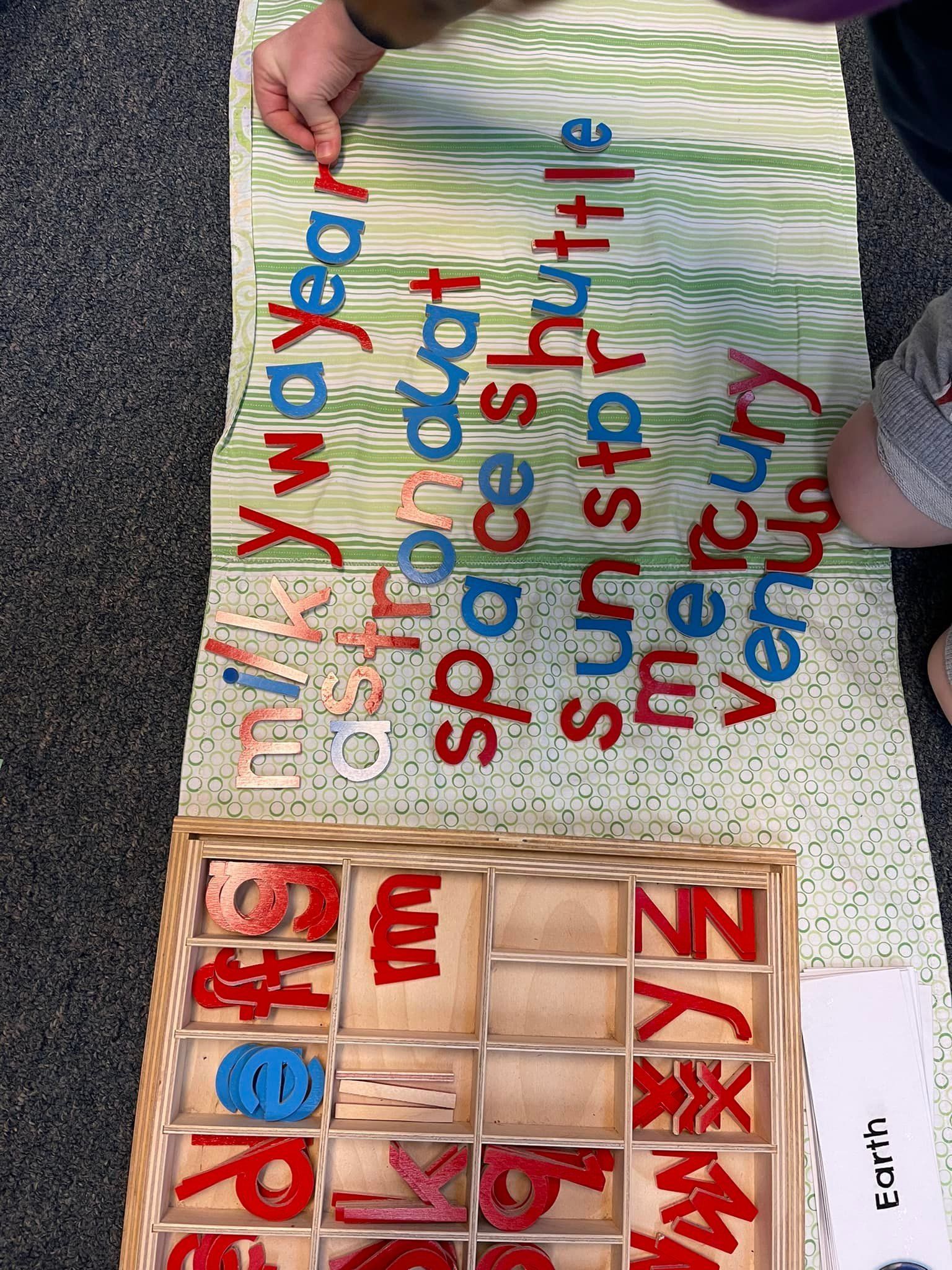 Person arranging red and blue wooden letters on a green-patterned cloth
