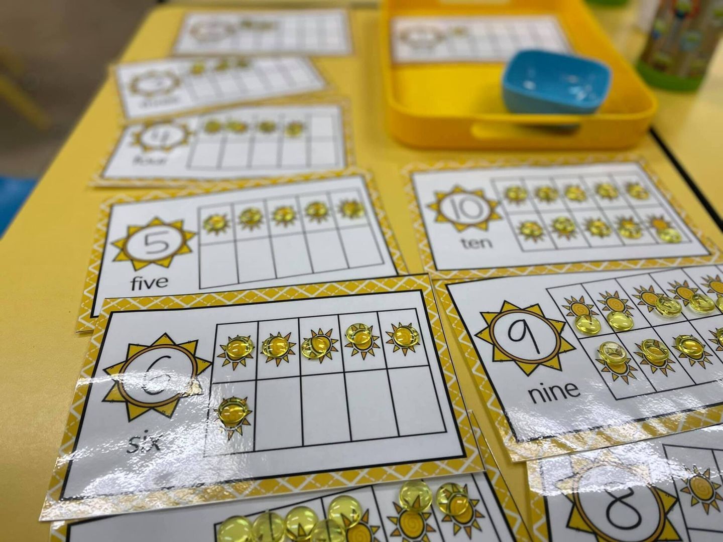 Yellow ten frame cards with sun-shaped counters on a yellow table