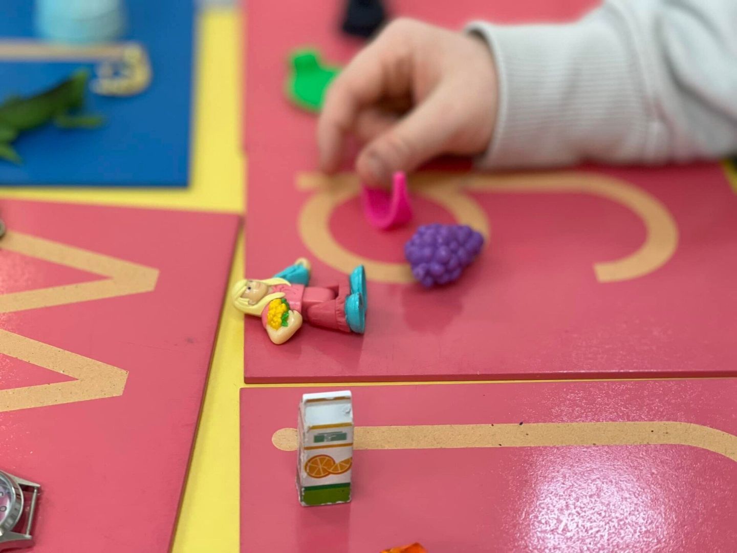 Child's hand interacting with toy figurines on pink and yellow letter boards