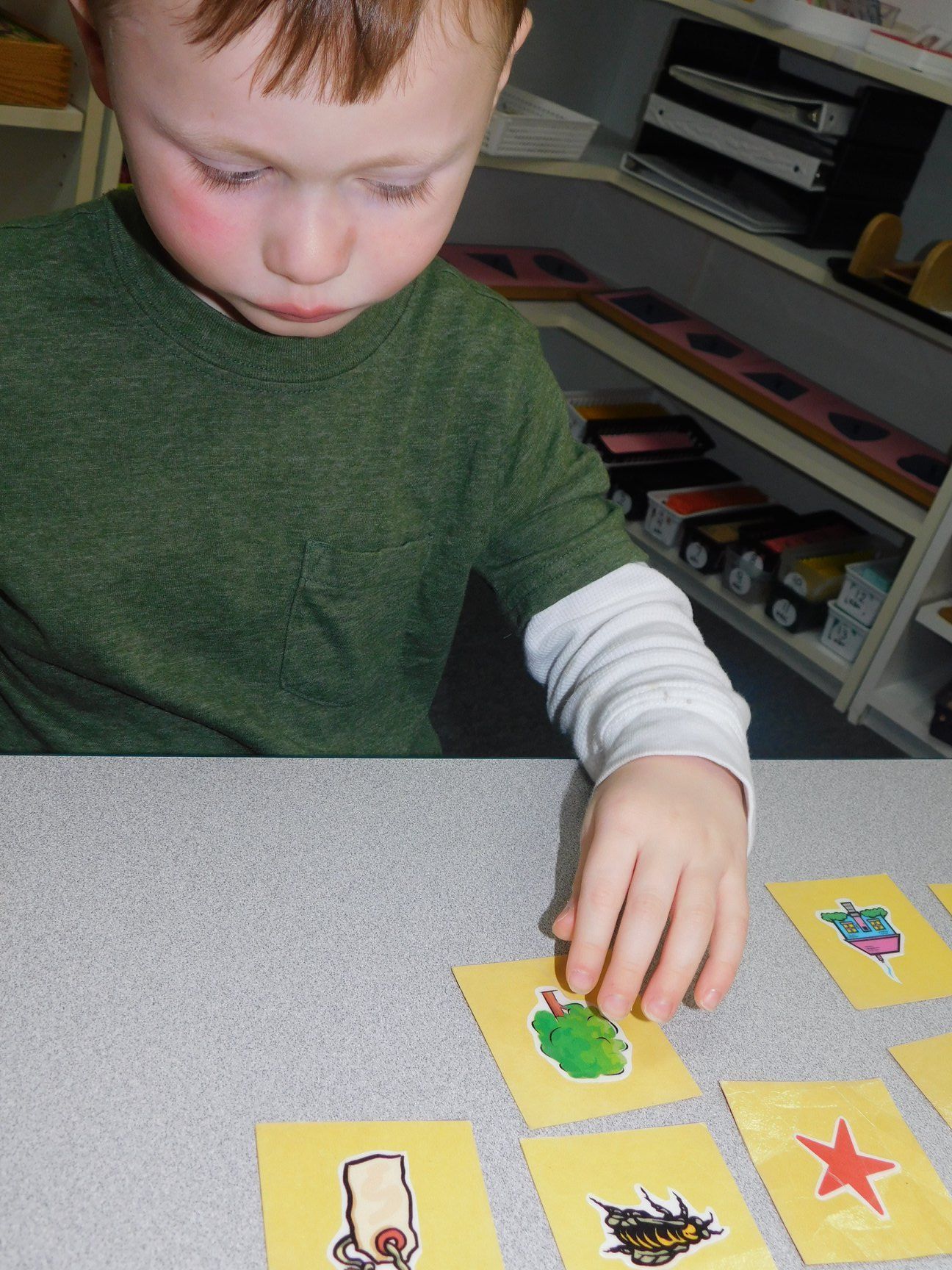 Boy in green shirt looks at yellow cards with drawings on a table