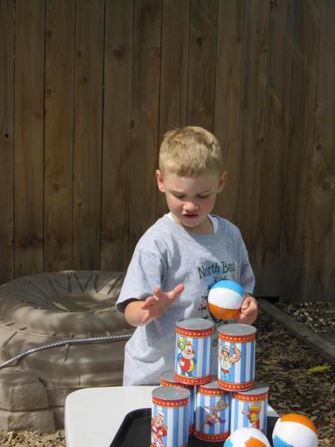 Boy throwing a ball at a pyramid of cans, outside