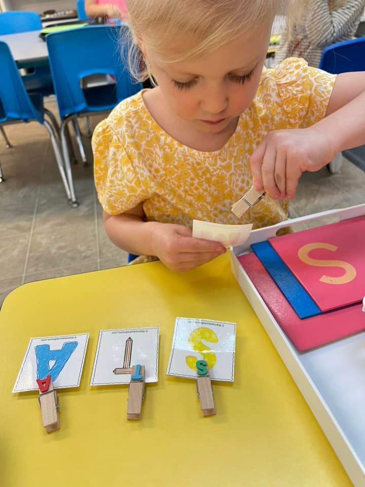 Girl using a clothespin to match letter cards on a yellow table