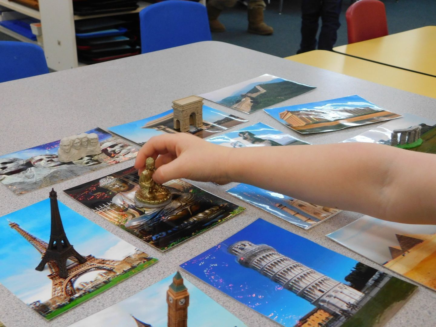 A child's hand placing a small statue on a postcard