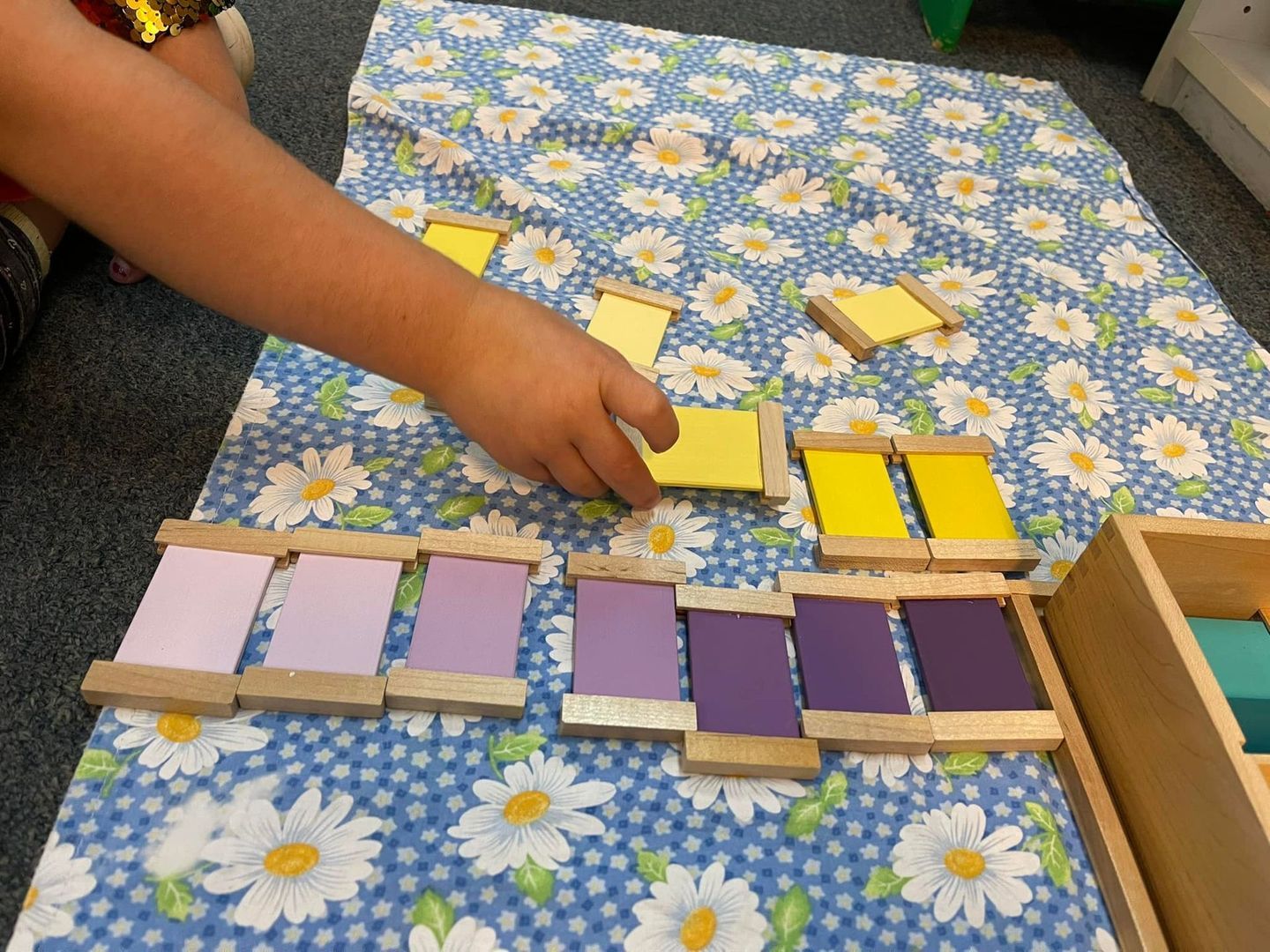 Child sorting colored wooden tablets on a blue floral surface