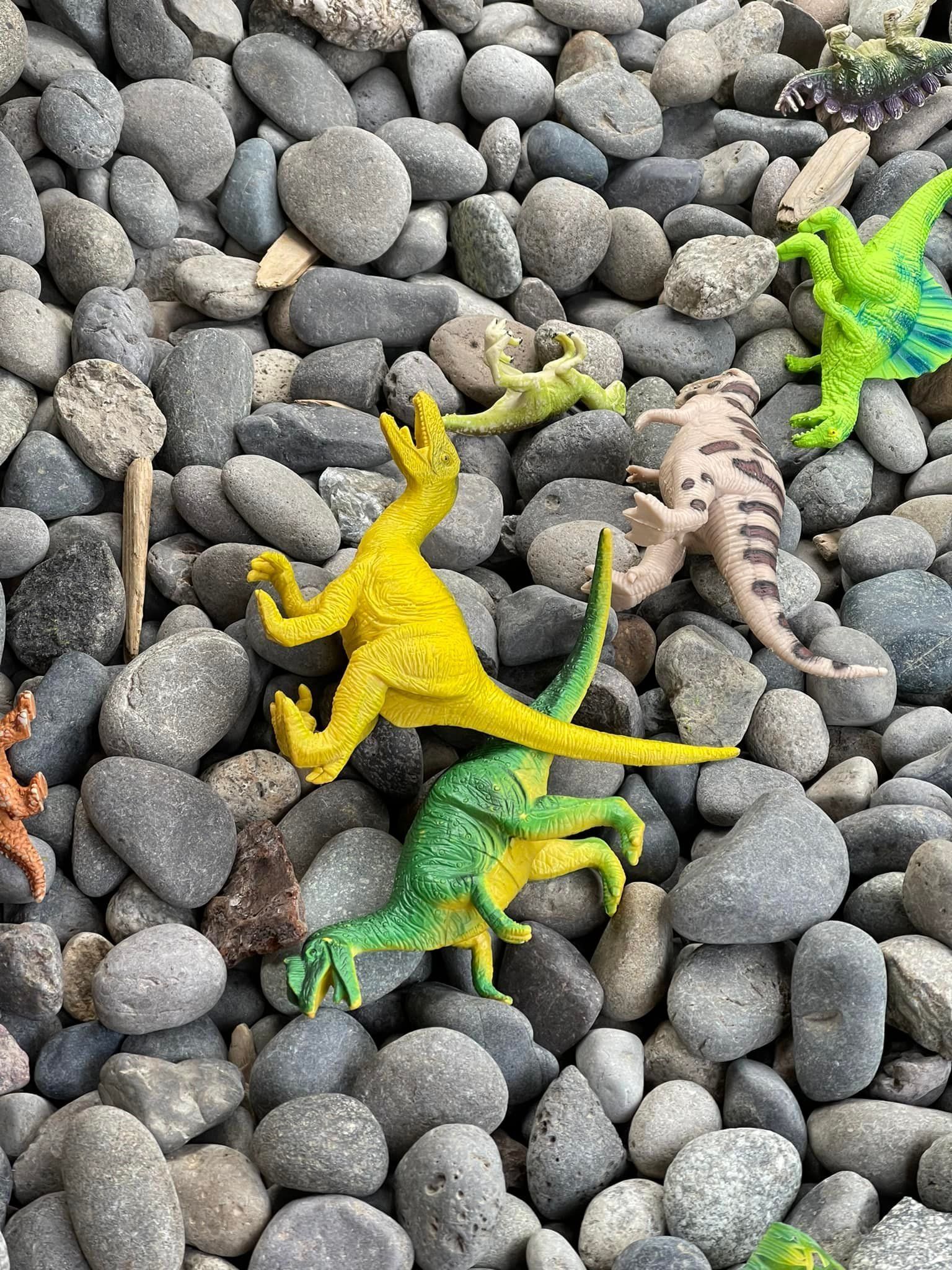 Toy dinosaurs in various colors scattered on a bed of gray stones