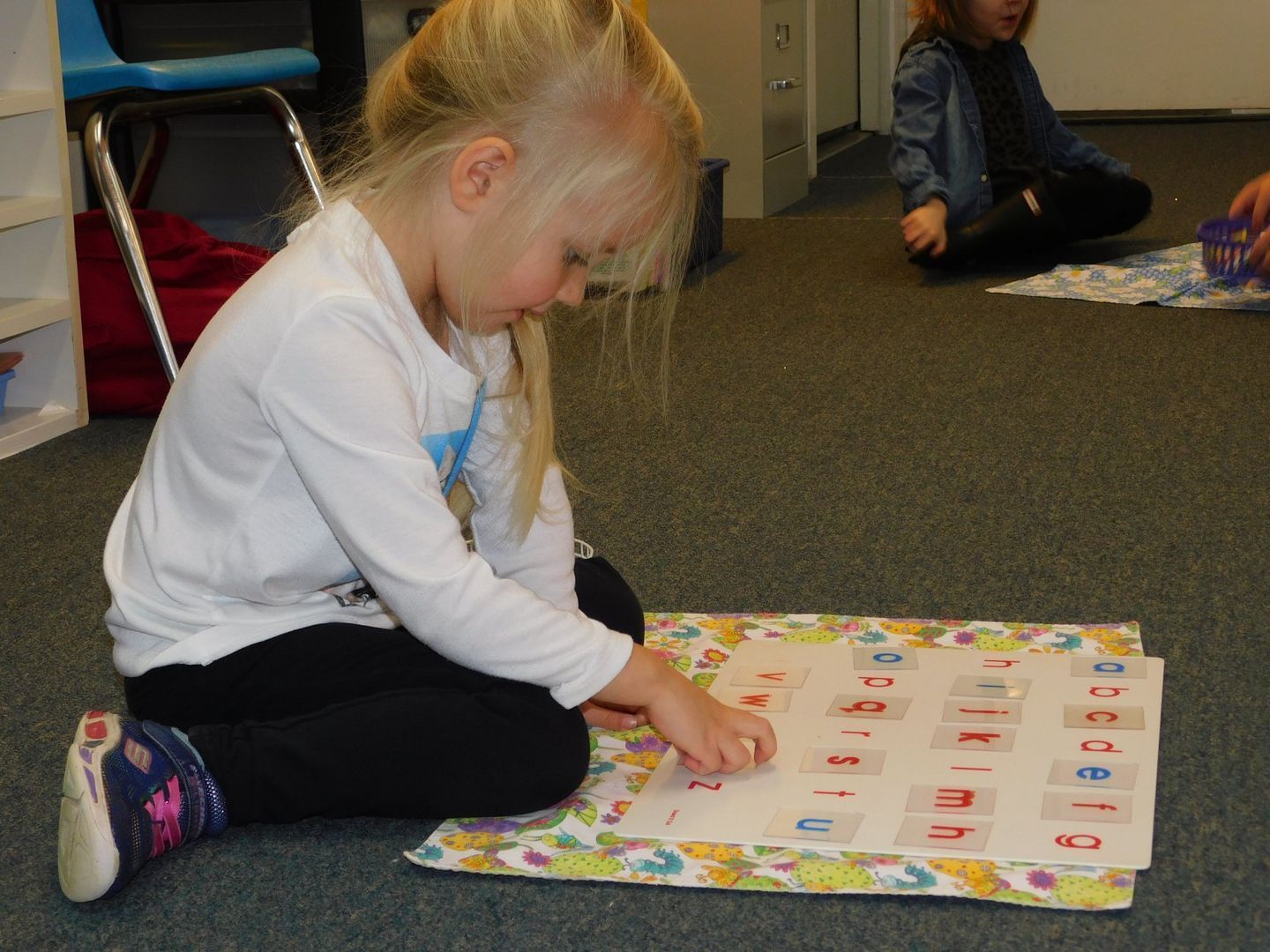 A young girl with blonde hair sits on the floor