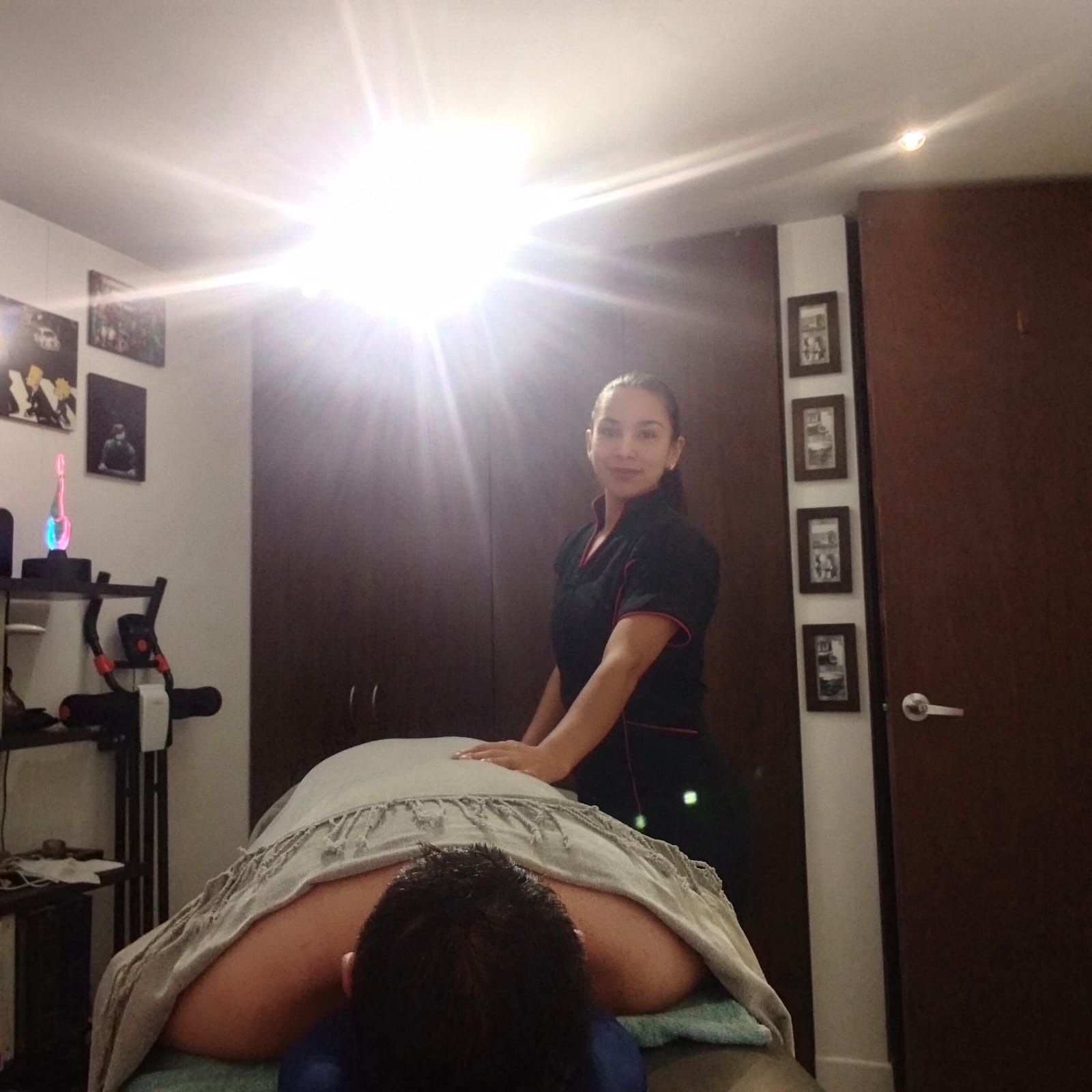 Escena de masaje terapéutico en una habitación, con un cliente tumbado boca abajo y un profesional de pie cerca.