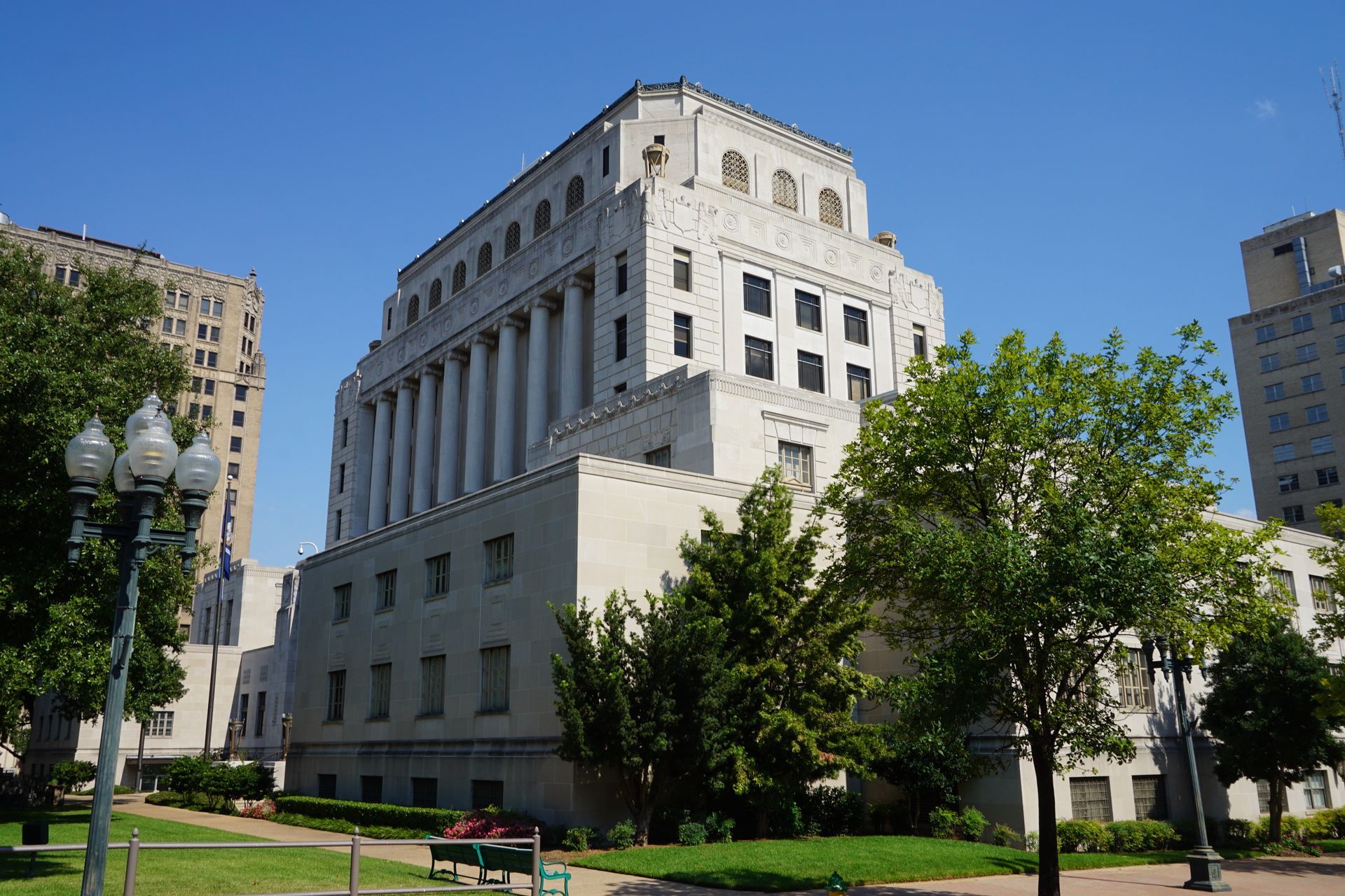White stone office building with columns and trees in a sunny city park