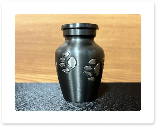 Black decorative vase with leaf engravings on a dark surface against a wooden background