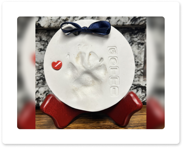White round ornament with red heart, navy bow, and paw print on red stand against a stone background