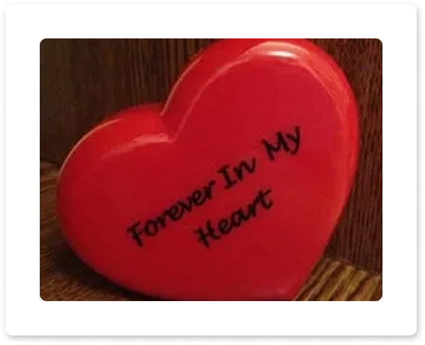 Red heart-shaped ornament with the words “Forever in my heart” written on it.