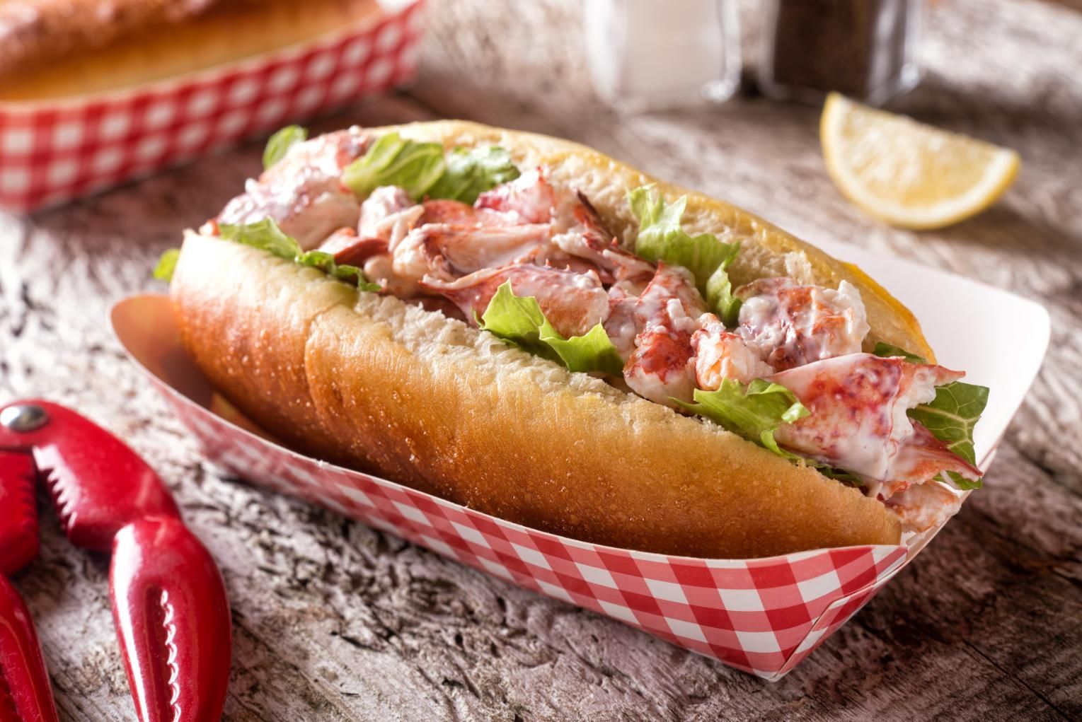 Hot dog topped with lettuce, bacon, and creamy sauce on a red-checkered tray liner