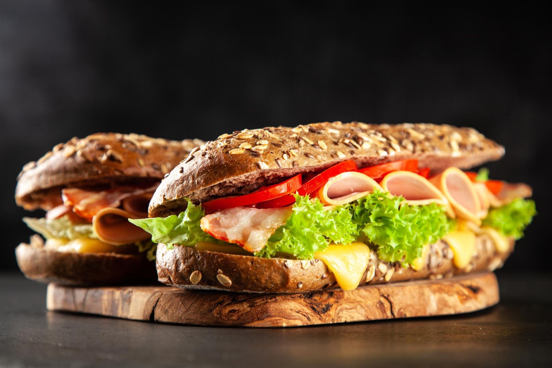 Two stacked deli sandwiches with lettuce, tomato, and meat on a wooden board