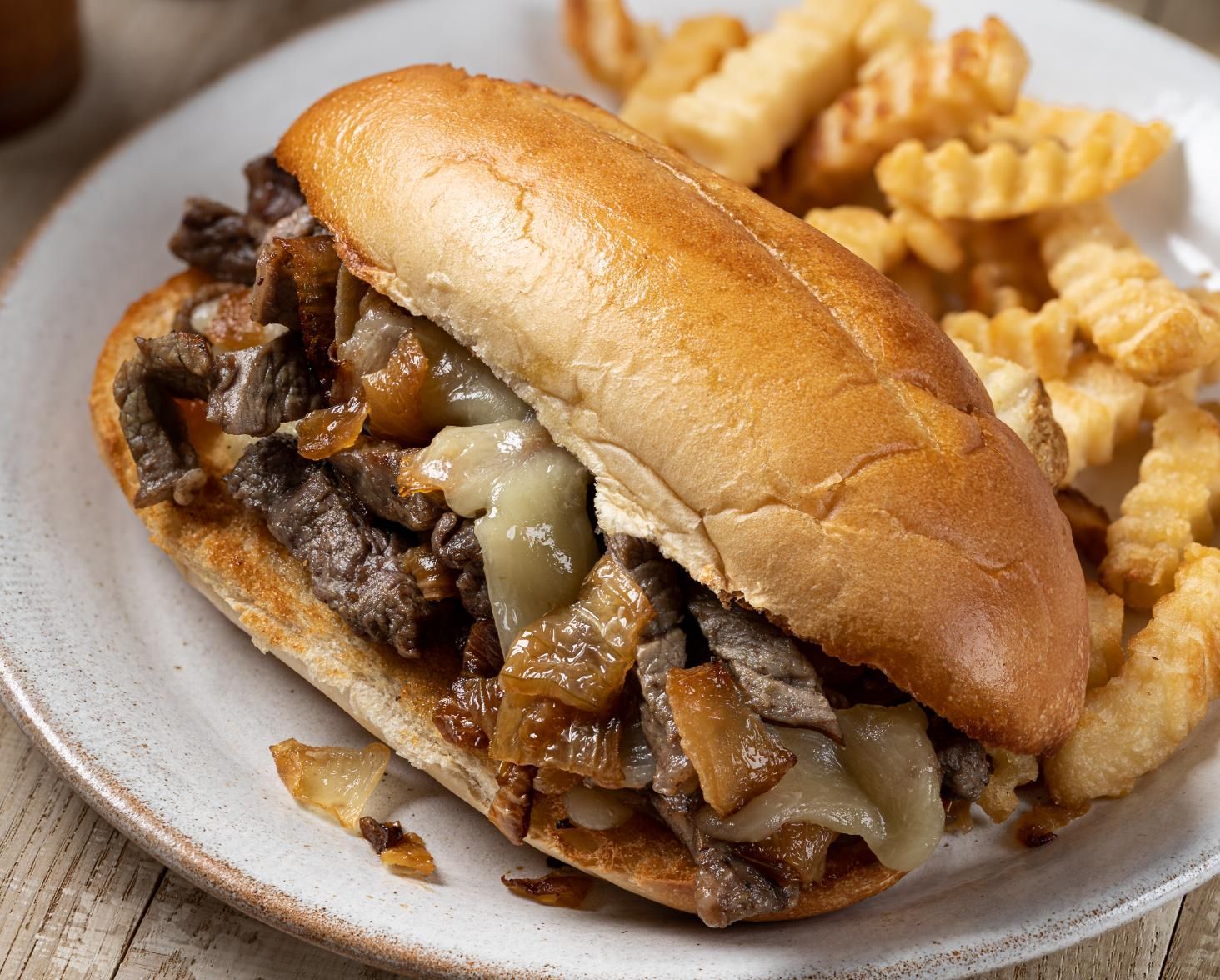 Cheesesteak sandwich with crinkle-cut fries on a plate