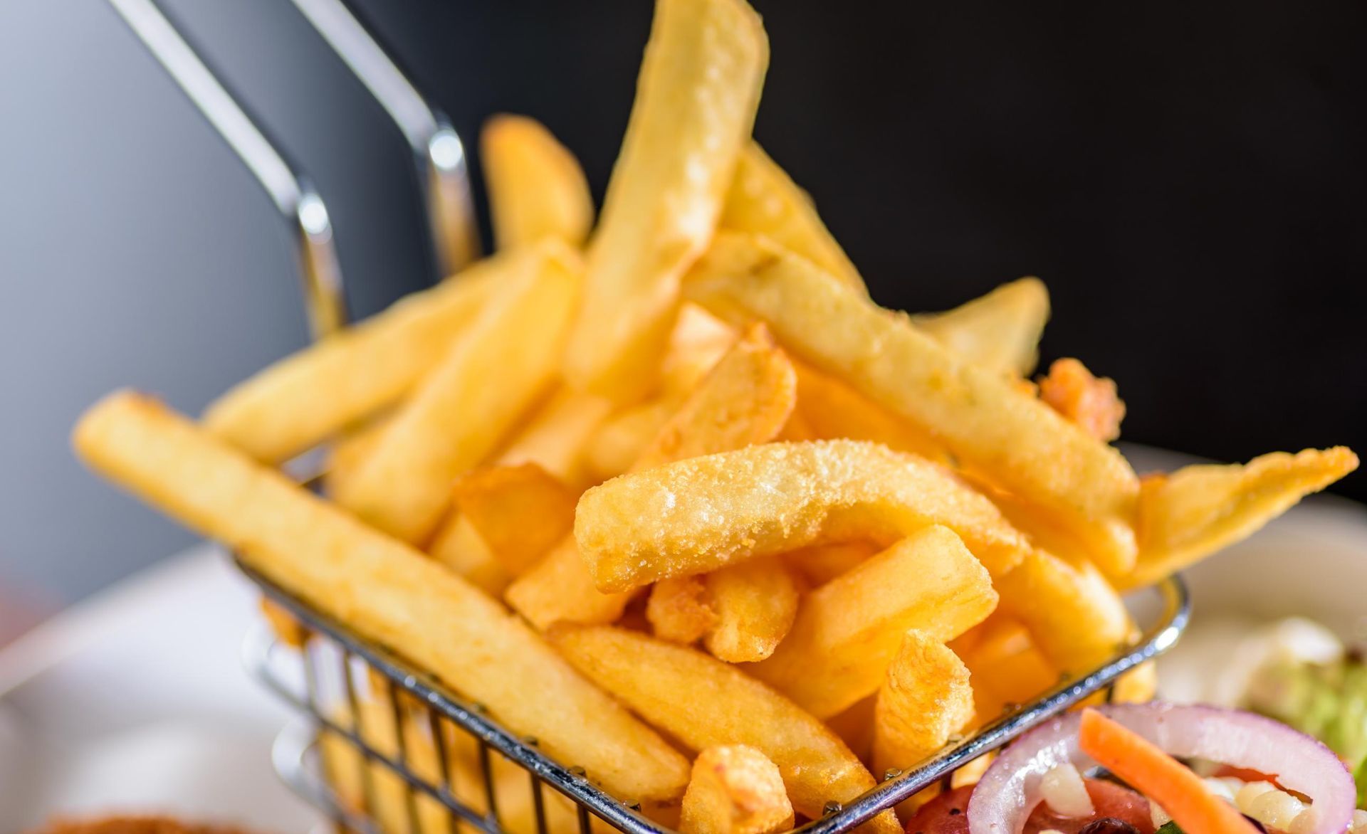 Basket of golden French fries with a side of ketchup and onions