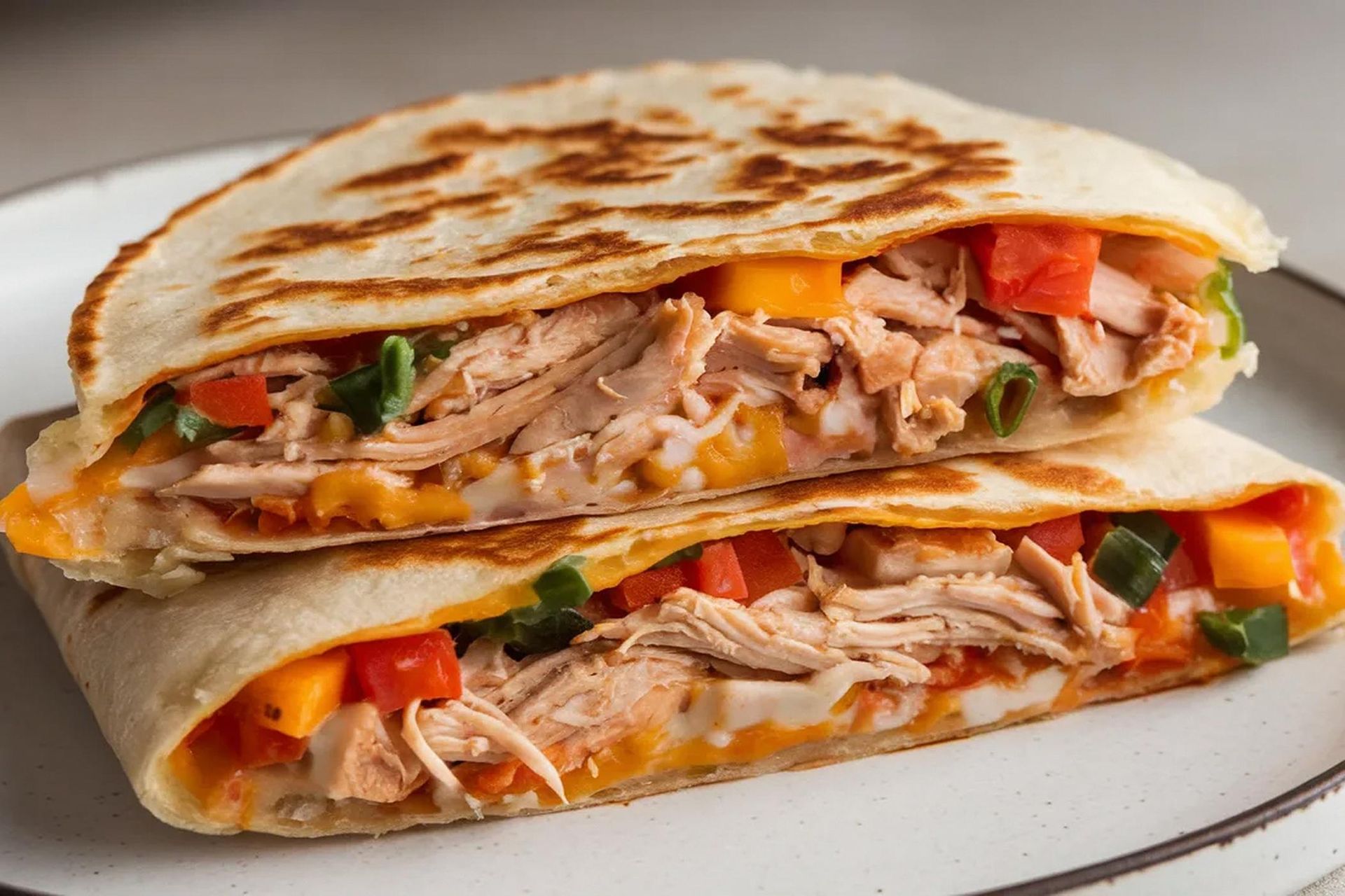 Grilled chicken and vegetable wraps stacked on a white plate