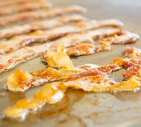 Close-up of golden-brown bacon strips sizzling on a griddle