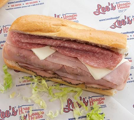 Sub sandwich with ham, salami, and cheese on branded deli paper.