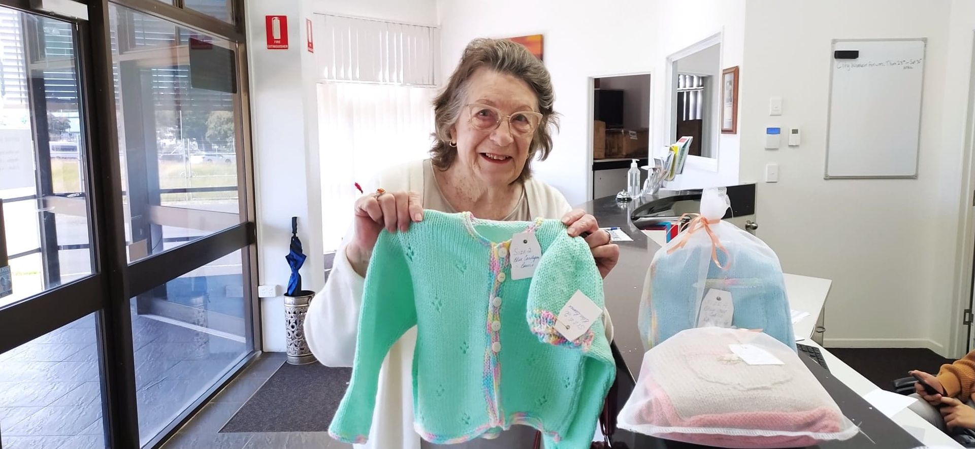 An elderly woman is holding a green sweater in a room.
