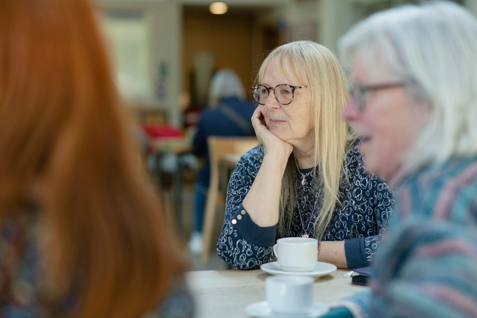 A group of women are sitting at a table with cups of coffee.