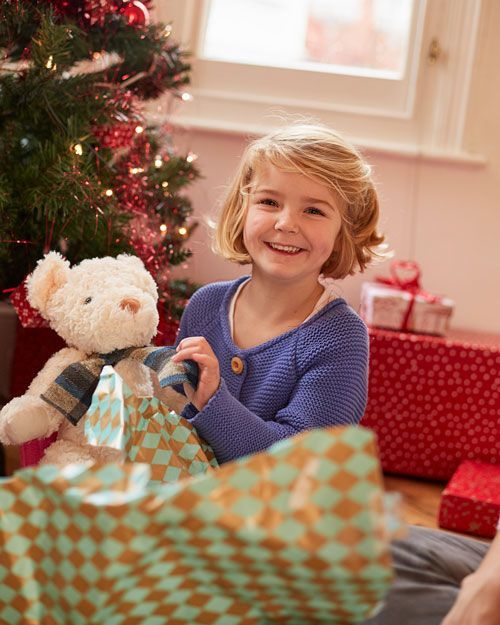 A little girl is opening a christmas present in front of a christmas tree.
