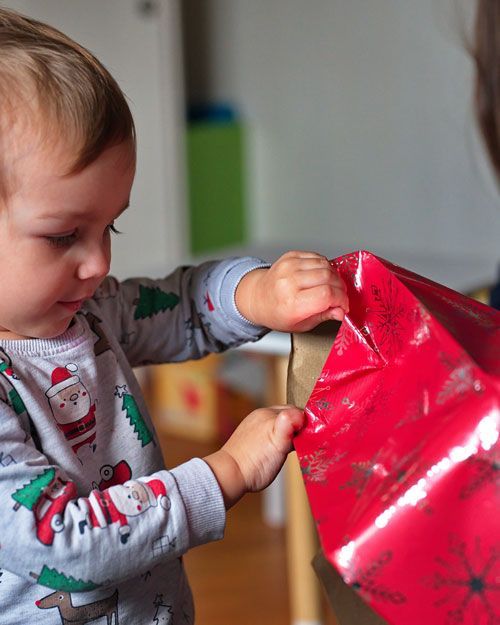 A little boy is opening a red christmas present.