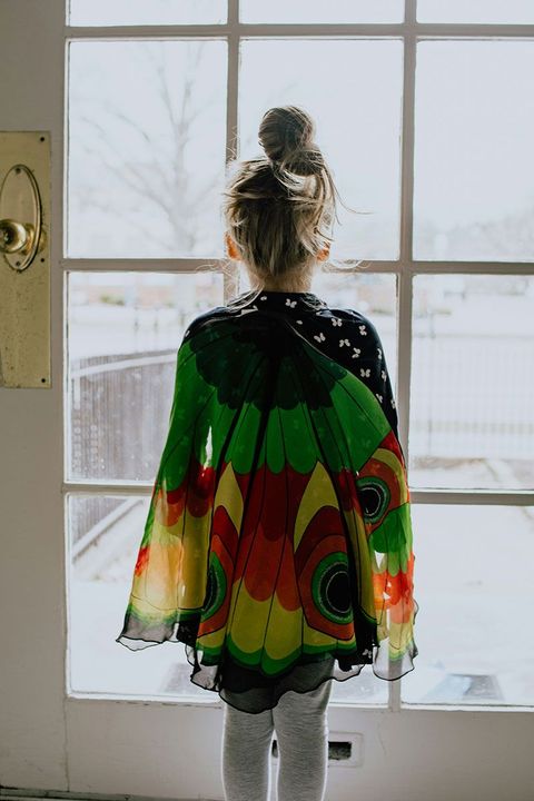 A little girl is standing in front of a window looking out.