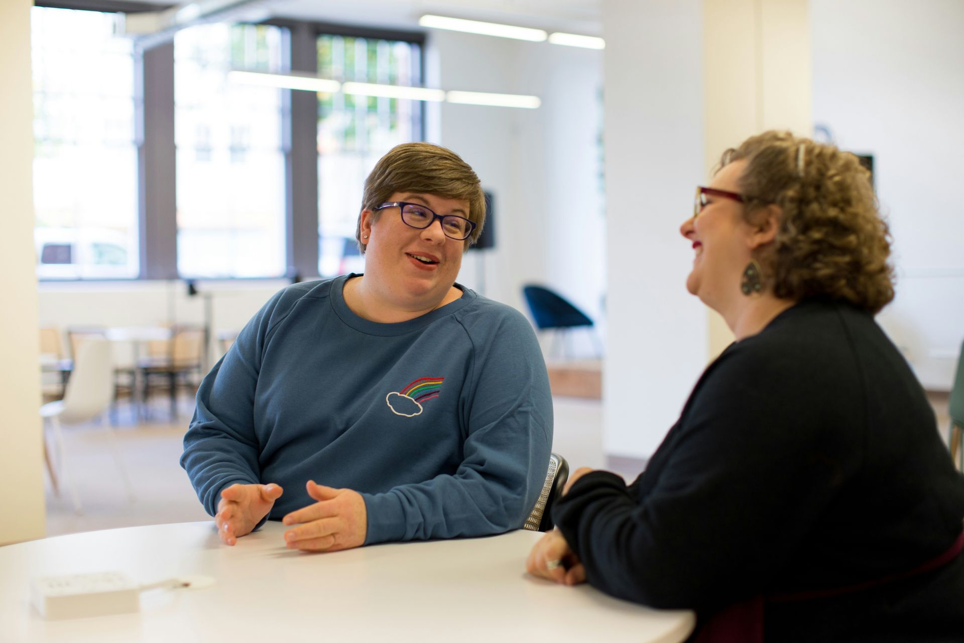 Two women are sitting at a table talking to each other.