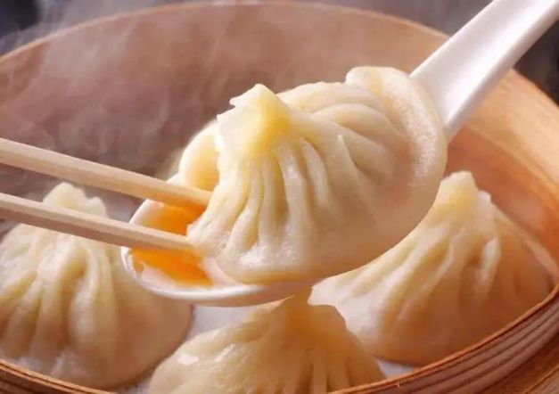Steamed dumplings being picked up with chopsticks from a bamboo basket