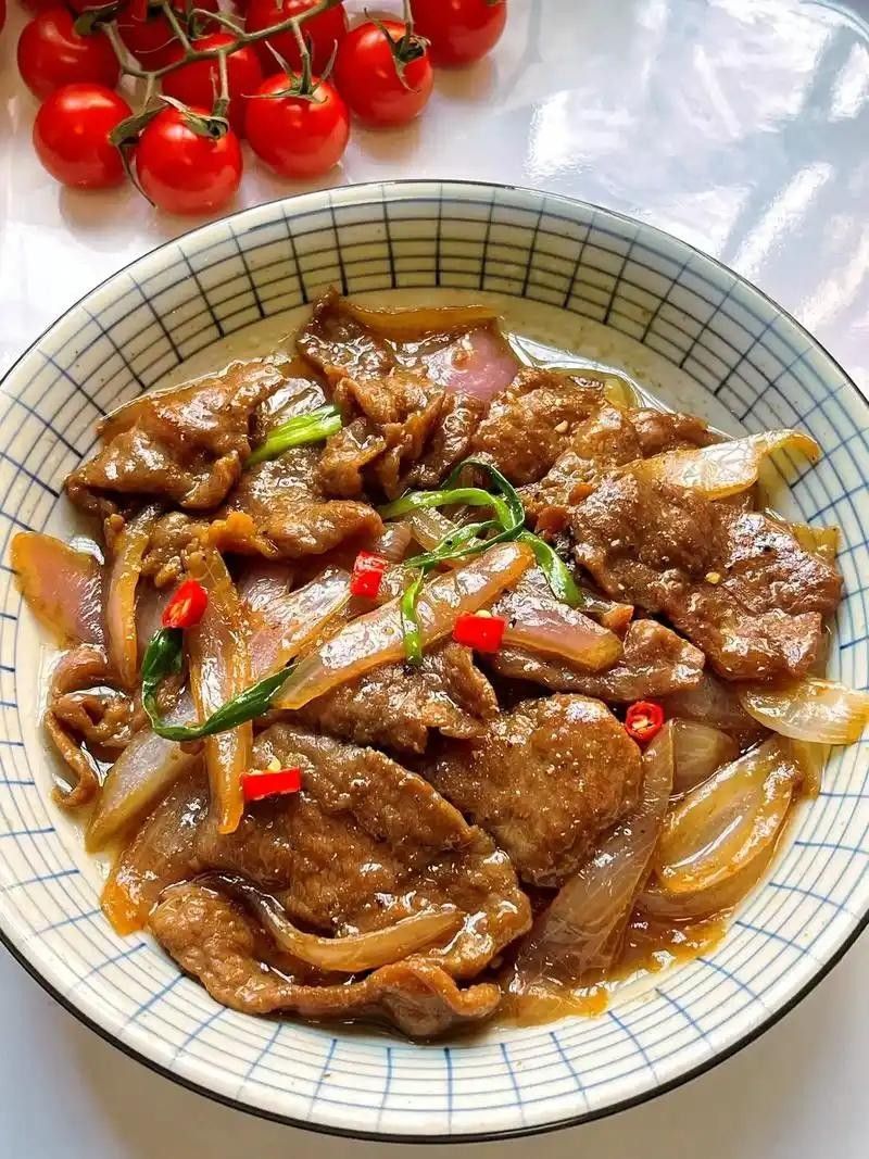 Braised meat with onions and red chili in a bowl, with cherry tomatoes beside it