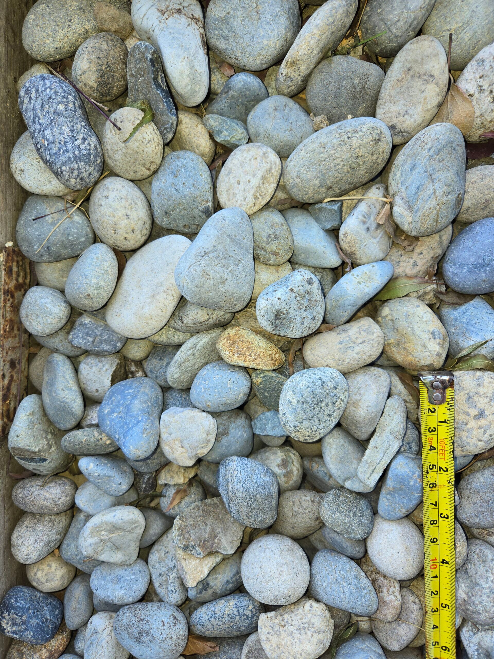 A pile of smooth gray pebbles with a yellow measuring tape along the right edge.