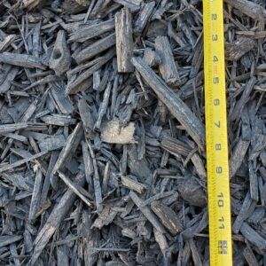 Pile of dark wood mulch beside a yellow measuring tape showing size in inches
