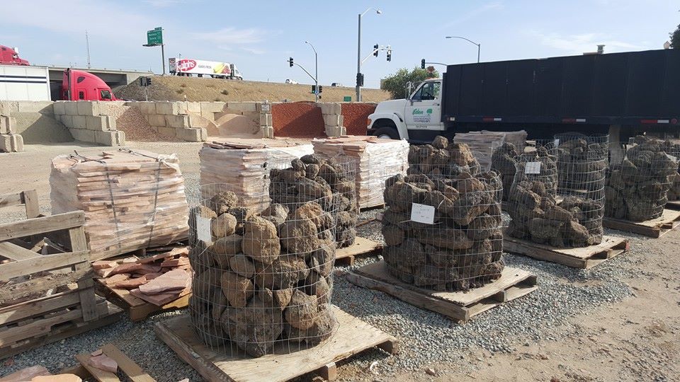 Stacks of stone blocks on pallets in an outdoor construction yard, with a truck nearby.
