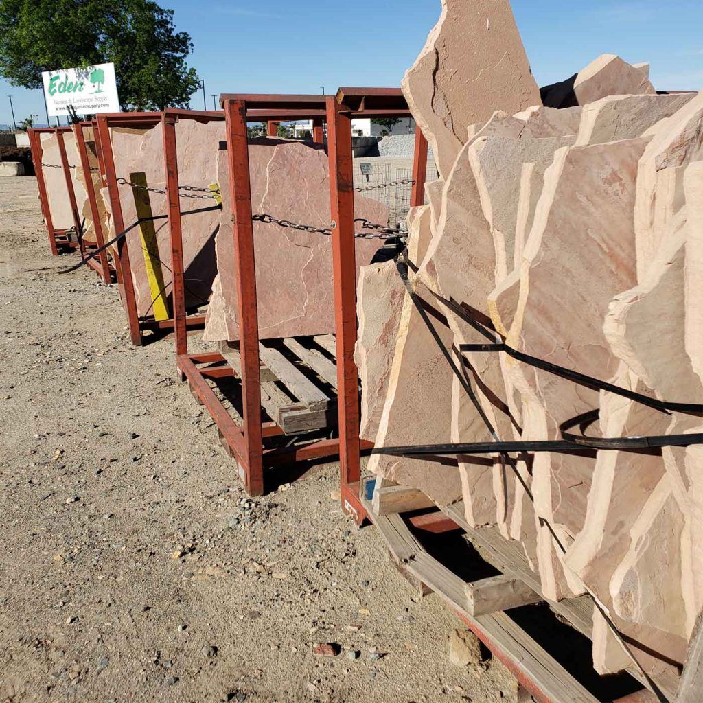 Large tan stone slabs strapped to red metal racks on pallets in an outdoor yard under a blue sky