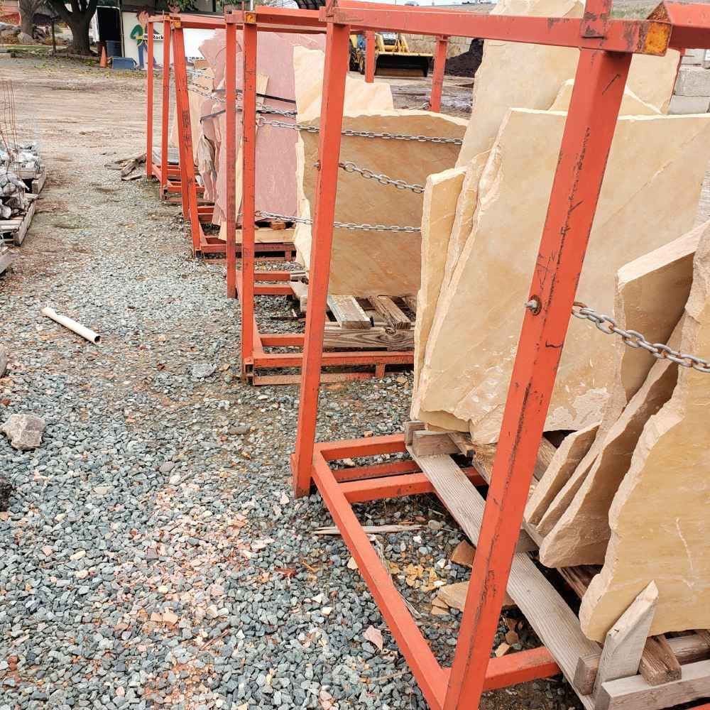 Orange metal racks holding large stone slabs on a gravel surface outdoors