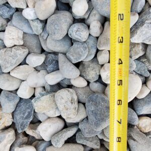 Pile of gray and white rocks beside a yellow measuring tape marked in inches