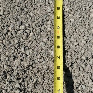 Yellow measuring tape standing in gray gravel, showing a close-up surface depth check