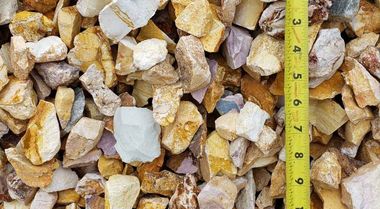 Pile of tan and white crushed stones with a yellow measuring tape along the right edge.