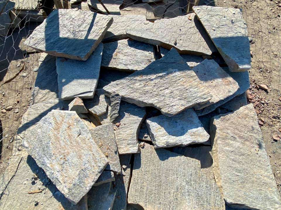 Stack of gray stone slabs and paving pieces on the ground outdoors.