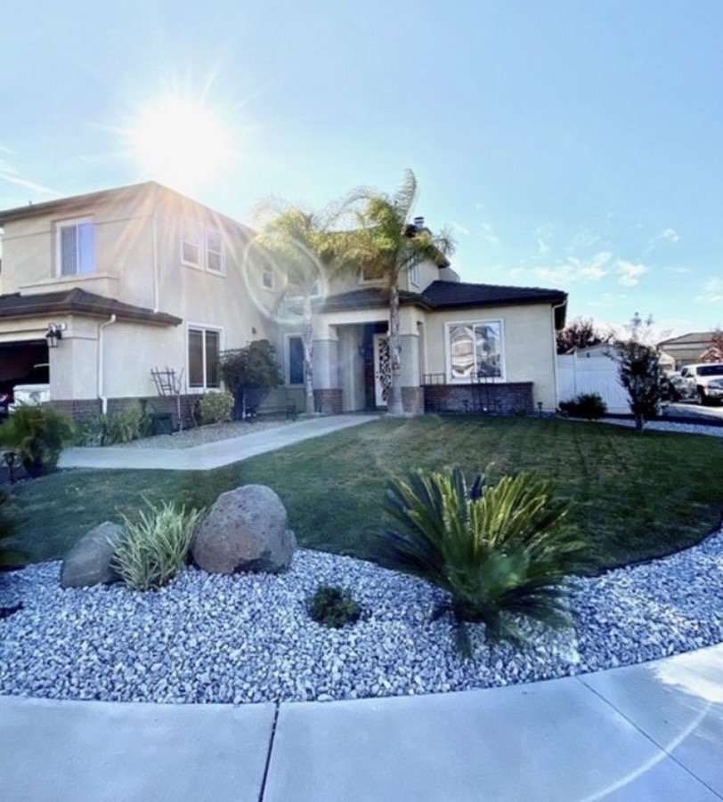 Suburban house with a manicured lawn, gravel landscaping, and bright sun in a clear blue sky