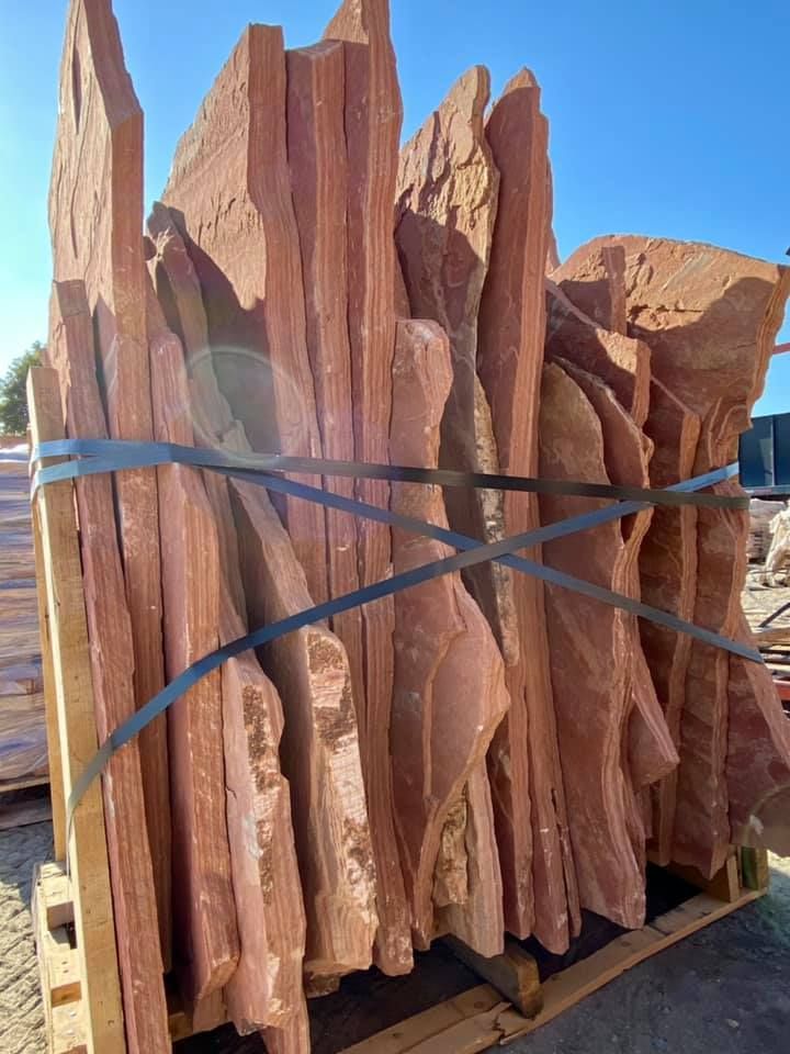 Stacked reddish stone slabs tied with blue straps on a wooden pallet outdoors.