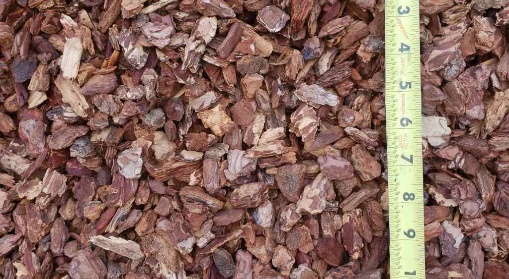 Close-up of reddish-brown bark mulch with a measuring tape along the right edge.