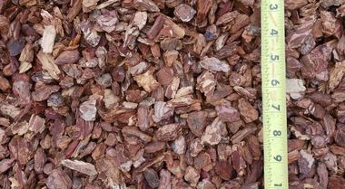 Close-up of reddish-brown wood chips with a vertical measuring tape along the right edge.