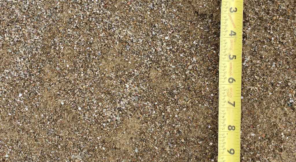 Close-up of granular brown surface with a yellow measuring tape marking height on the right.