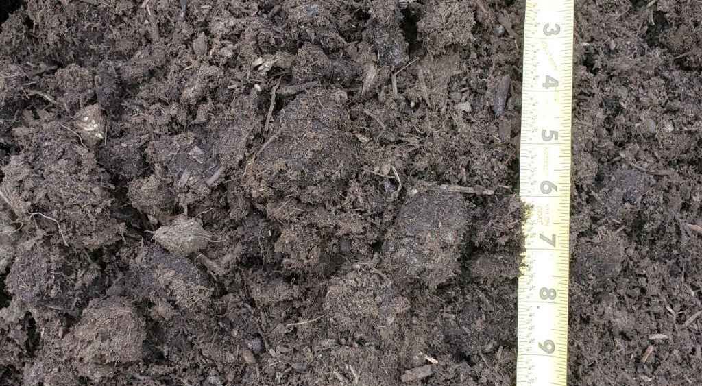 Close-up of dark soil or compost with a measuring tape along the right edge