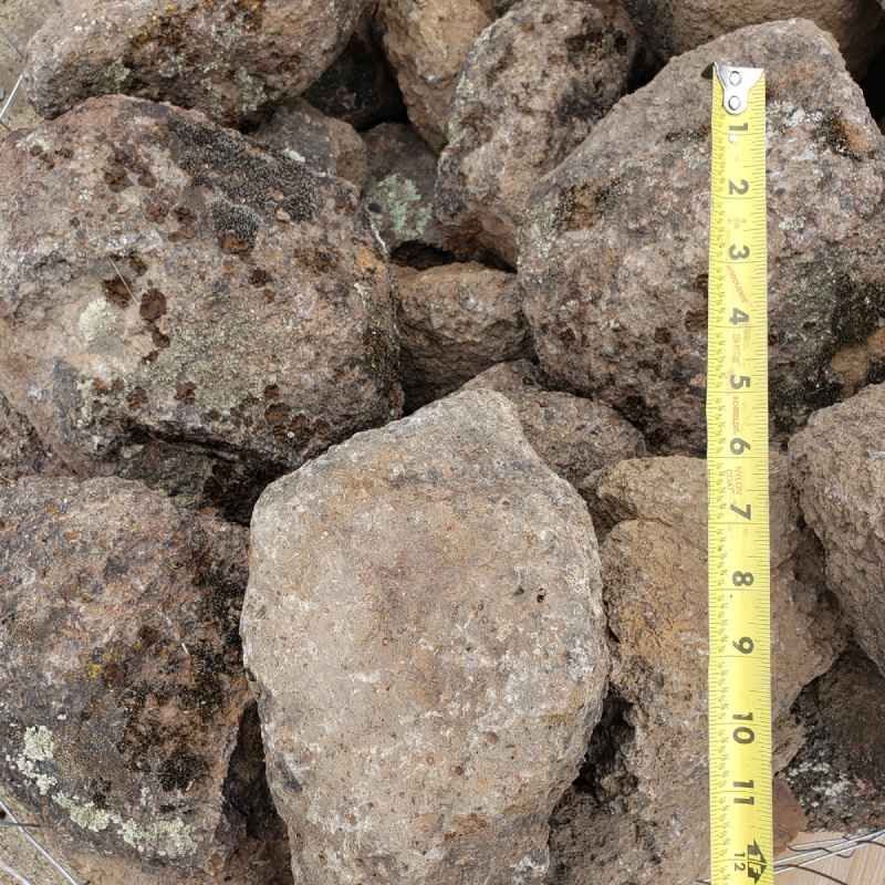 Pile of rough rocks with a yellow measuring tape showing their size